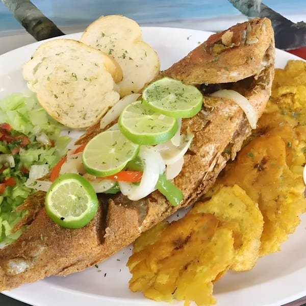 Whole fried fish with lime, onions, peppers, garlic bread, salad, and plantains from Willie's Pinchos.