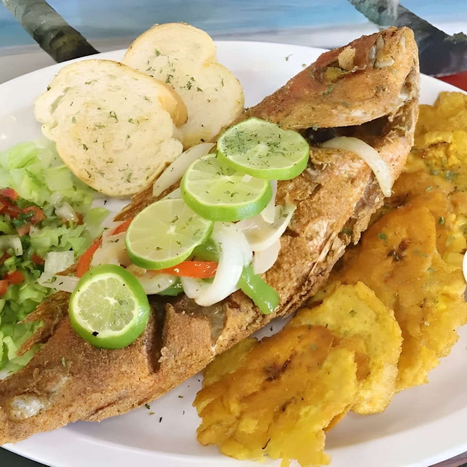 Whole fried fish with lime, onions, peppers, garlic bread, salad, and plantains from Willie's Pinchos.