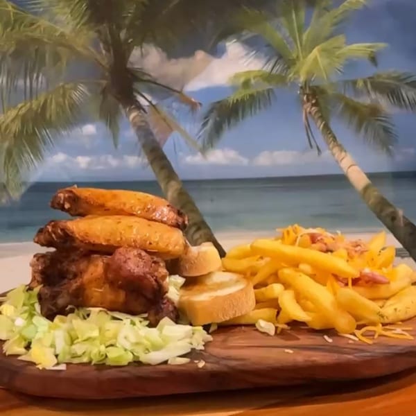 Willie's Pinchos' chicken wings, fries, and bread on a wooden board with a beach backdrop.