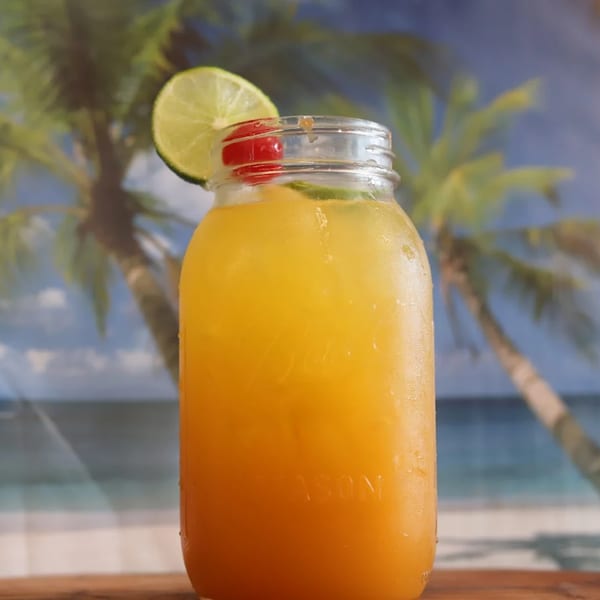 A refreshing Puerto Rican drink in a mason jar, garnished with lime and cherries, against a beach backdrop.