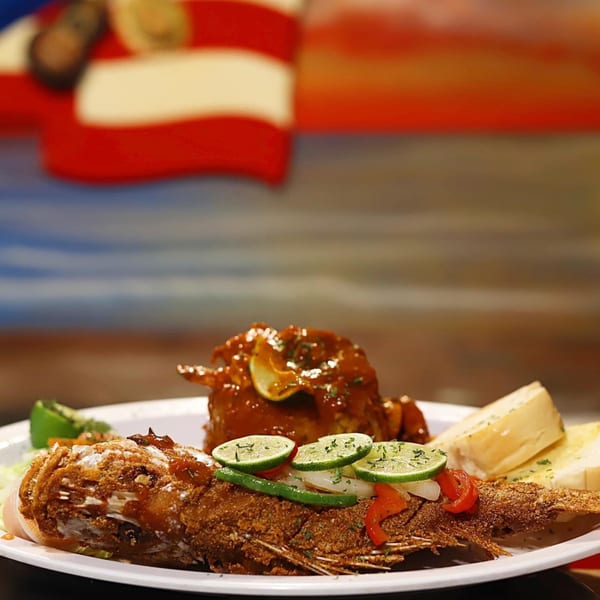 Whole fried fish topped with lime, peppers, and onions, served with bread and a side dish.
