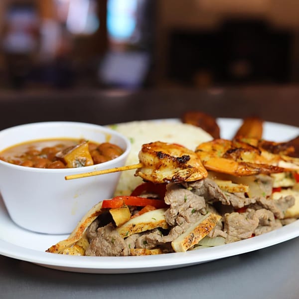 A Puerto Rican dish with grilled shrimp skewers, sliced meat, rice, and a side of beans.